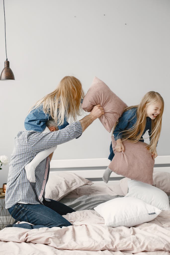 A joyful family bonding moment with a playful pillow fight in a cozy bedroom setting.